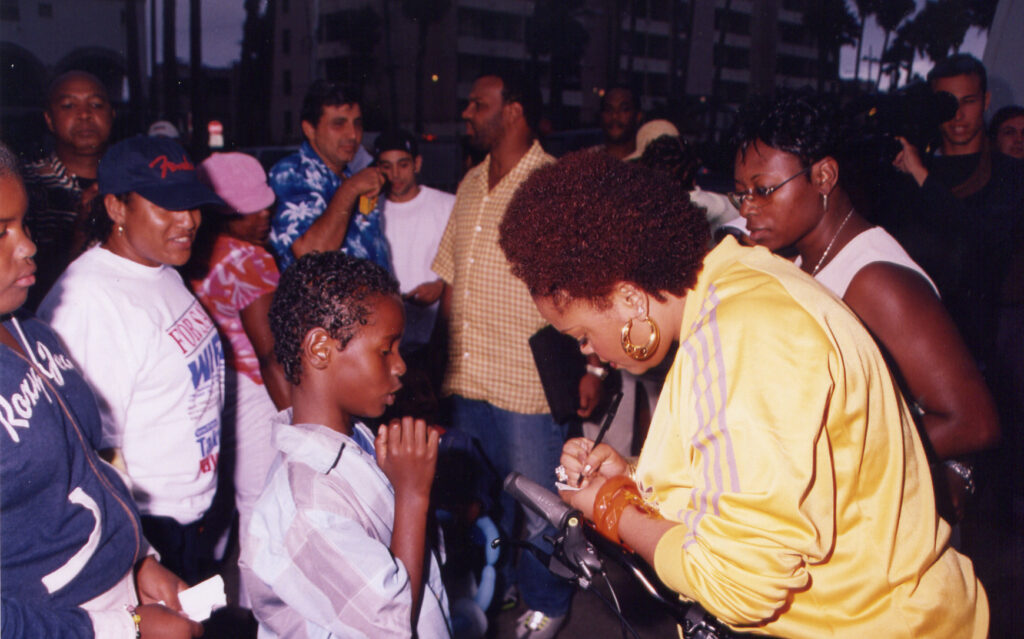 A behind the scenes photo of Jill Scott signing autographs on the set of her music video for her song "Golden" released by Hidden Beach Recordings